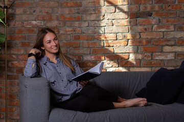 Woman in a dreamy mood on couch holding notebook