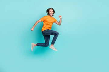 Fototapeta na wymiar Full length photo of confident excited man wear orange t-shirt jumping high running fast empty space isolated turquoise color background