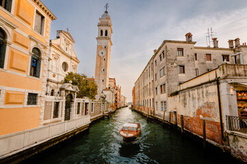 Typical Venetian boat as it sails past the church of San Giorgio dei Greci with its typical leaning bell tower