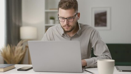 Concentrated young man using laptop, taking notes during remote lecture. Student studying online at home, looking at laptop screen