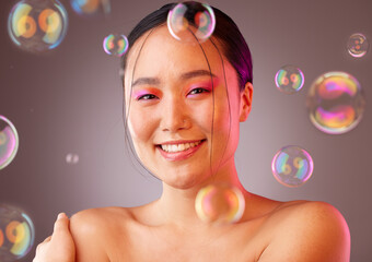 Makeup, bubbles and Asian woman with smile, for cosmetics, skincare or health on a studio background. Portrait of a young girl with body care, natural beauty or happiness for organic facial