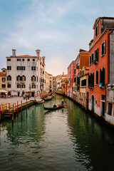 Venetian gondola as it sails on characteristic canal with colorful buildings at sunset