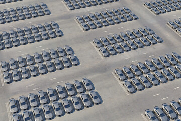 Aerial view of new electric sports cars on a huge car dealer parking lot. Multiple rows of self driving cars ready for import and export business. New cars in storage for sale. Realistic 3d rendering