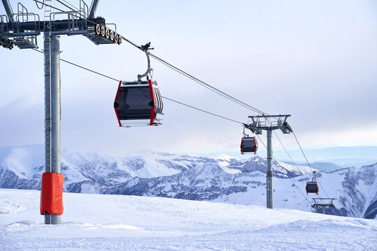 Cable car gondola at ski resort with snowy mountains on background. Modern ski lift with funitels and supporting towers high in the mountains on winter day. No people.