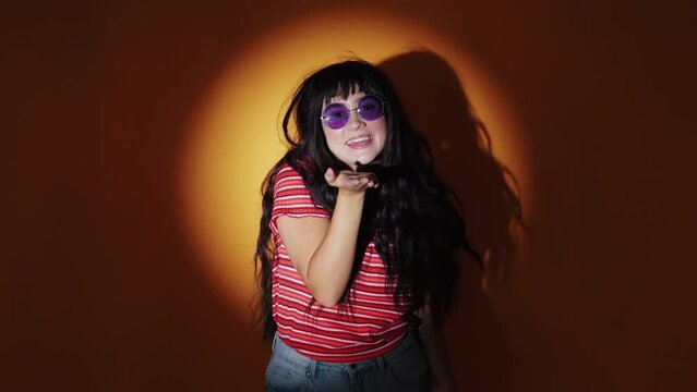 Casual Young Girl In Purple Lens Sunglasses, Blowing A Kiss Standing Against Warm Light Background. - Medium Closeup Shot