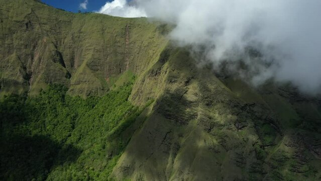 View from above, stunning aerial view of a green mountain range surrounded by clouds and a beautiful blue sky in the background. Sembalun, Lombok, West Nusa Tenggara, Indonesia. 