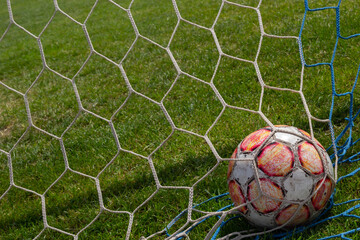 old soccer ball in the net on the background of grass soccer field. Summer sunny day