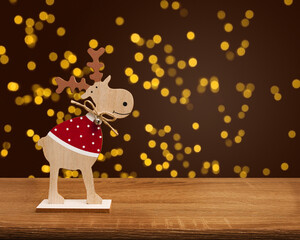 Obraz na płótnie Canvas A wooden Christmas deer stands on a wooden table on a blurry bokeh background. Blurred light gold bokeh.