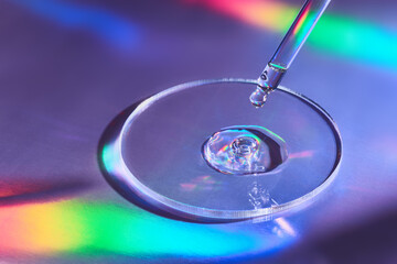 Pipette with sample of cosmetic product in petri dish on holographic background, iridescent...