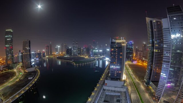 Cityscape panorama of skyscrapers in Dubai Business Bay with water canal aerial during all night timelapse. Modern skyline with illuminated towers and lights turning off. A center of international