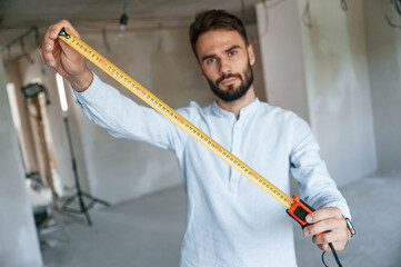 Holding ruler measurement tool. The man is making repairs in the apartment