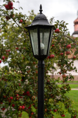 Street lamp in the garden. Against the background of an apple tree with red apples.