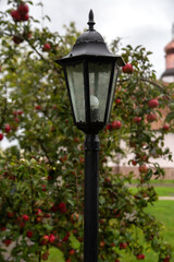 Fototapeta na wymiar Street lamp in the garden. Against the background of an apple tree with red apples.