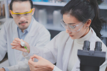 Asain Female scientist is focusing and looking while dropping green substance in laboratory eco or...
