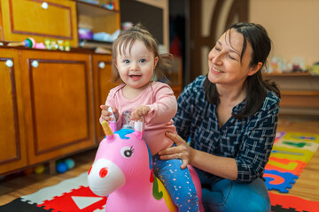 Baby who stands on a toy horse, unicorn and playing with his mother