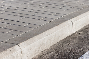 The sidewalk paved with concrete tiles is separated from the asphalt road by a concrete curb.
