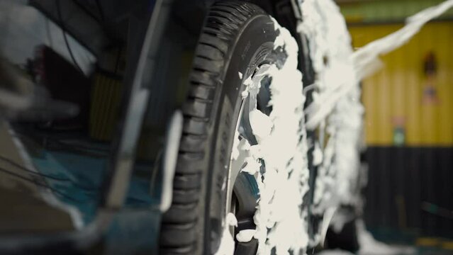 Close-up car wash foam worker washing car and wheel service. Car wash cleaning station high pressure water. Employees clean a dirty vehicle professionally. Self-service car wash.
