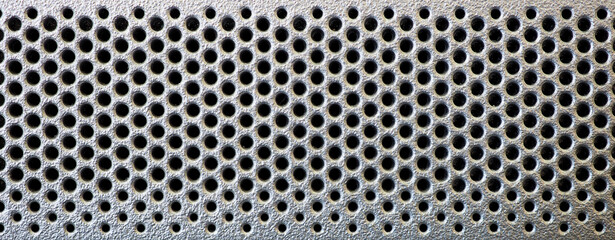 Grid in the form of round holes in a silvery plastic panel. Perforated surface with mesh pattern....