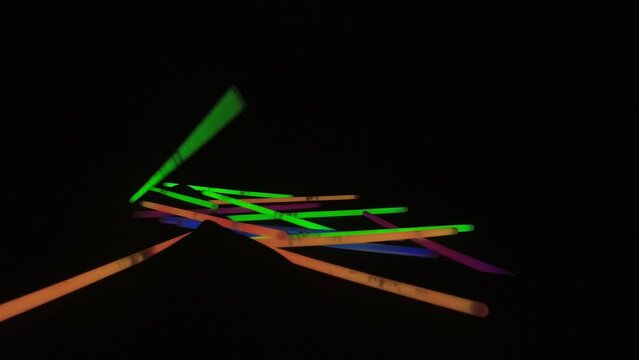 Glowing neon light sticks are dropped in darkness onto black surface