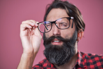 Checking his glasses, shortsighted bearded man examining his spectacles, blurred person behind the...