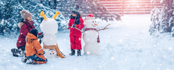 Family bilding a cute snowman in the snowy park. - 541208204