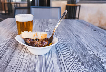 Close-up photo of a fresh beer in a glass and an aperitif of a serving of pork cheeks.