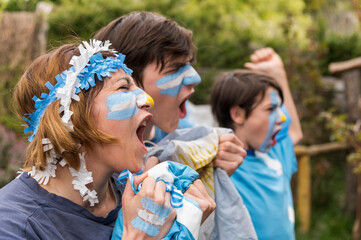 Familia maquillada con los colores del equipo Argentino gritando el gol.  - obrazy, fototapety, plakaty
