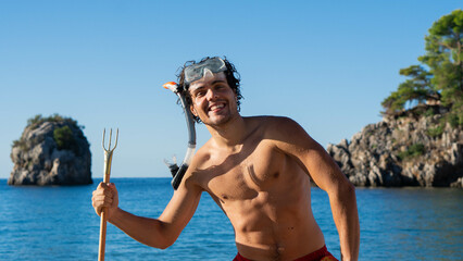Muscular young smiling man posing with snorkeling mask and harpoon with the sea at the background. Swimming, diving, vacation concept.