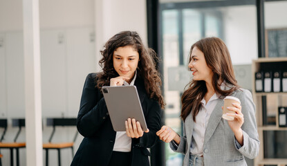 Businesswomen work and discuss their business plans. A Human employee explains and shows her colleague the results paper in modern office..