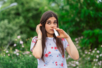Pollen allergy concept. Young woman using nose spray for her pollen and grass allergies. Flowering...