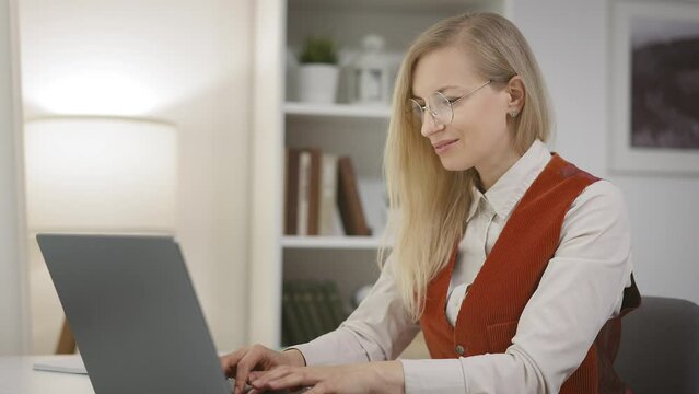 Successful felame freelancer working from home, typing on laptop keyboard and smiling. Businesswoman concluding deal.