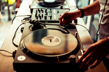 Dj hands on equipment deck and mixer with vinyl record at party, human hands using two vinyl turn...