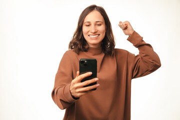 Fototapeta premium Photo of joyful young woman smiling and looking at smartphone and celebrating victory