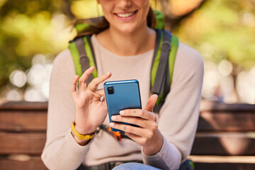 Phone, hands and hiking woman relax outdoors check hike trail online using 5g tech internet device. Young girl smile, search travel direction or type social media smartphone communication in nature