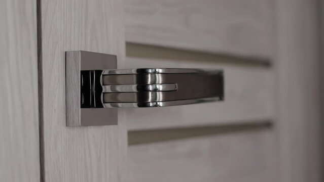 The silver door handle is pressed by itself. The man inside presses the doorknob, close-up