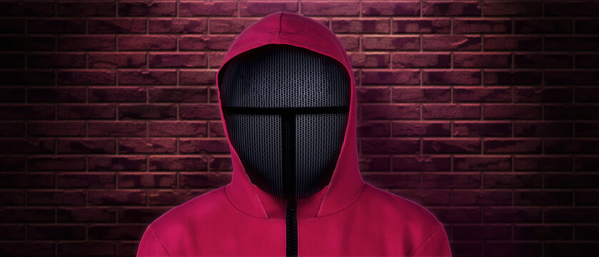 A Black Mask Of A Security Guard In A Red Jumpsuit Based On The Famous Korean Game And TV Series. Brick Wall.