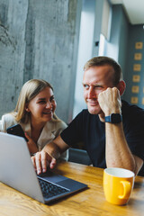 Positive young colleagues managers sitting at the table and laughing looking at the laptop. Teamwork concept. Selective focus. Modern successful people