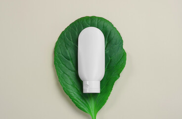 White plastic tube with hand, face, body cream on a large green leaf. Beauty skin care product template. White tube on a green leaf