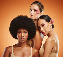 Makeup, women and beauty, diversity and flowers on orange studio background. Models, skincare and friends together with serious facial expression, organic cosmetics or empowerment with floral orchids