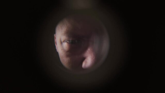 A male apartment burglar stands on the stairwell and peers through the peephole, close-up. The concept of theft in apartments.