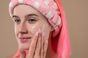 Cute pink-haired girl putting cream on her face