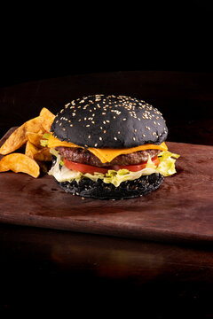 halloween themed burger tomato, black bun lettuce with gergilin on cattail with rustic potatoes isolated on front closeup
