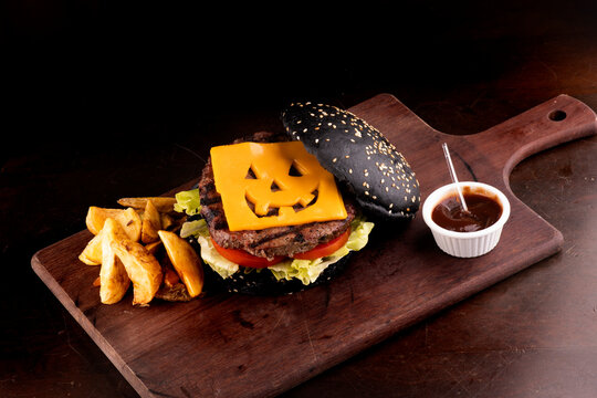 halloween themed burger with funny cheddar cheese and black bun with gergilin on cattail and dark background angle view