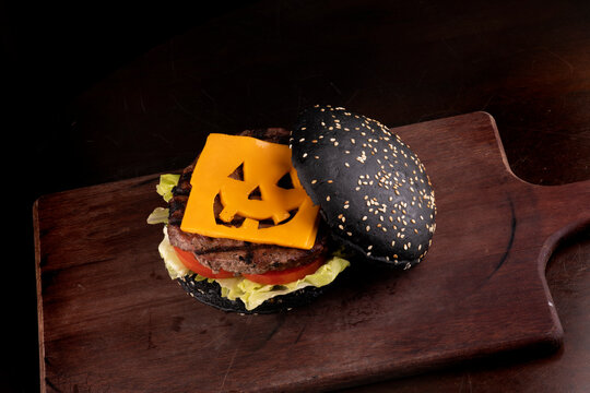 halloween themed burger with funny cheddar cheese and black bun with gergilin on cattail and dark background top view