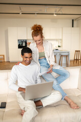 Obraz premium Young man with a laptop sitting on the sofa, his wife standing next to him