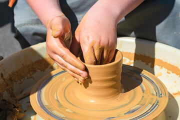 Hands of a child making a piece of clay behind a potter's wheel