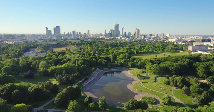 Pole Mokotowskie Warsaw Park field with lake and city skyscrapers in the background. Aerial view of the city park with lake and green trees. Summer season.
