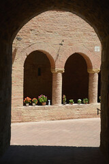 Fototapeta na wymiar Cloister with ancient brick arches and flowers in the heart of Tuscany.