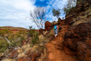 backpacker girl hiking on red rocks up a steep mountain in karijini national park in western australia, desert landscape of australian outback