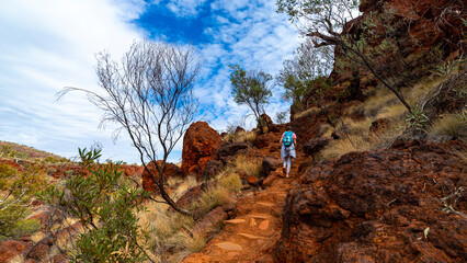 backpacker girl hiking on red rocks up a steep mountain in karijini national park in western australia, desert landscape of australian outback - Powered by Adobe
